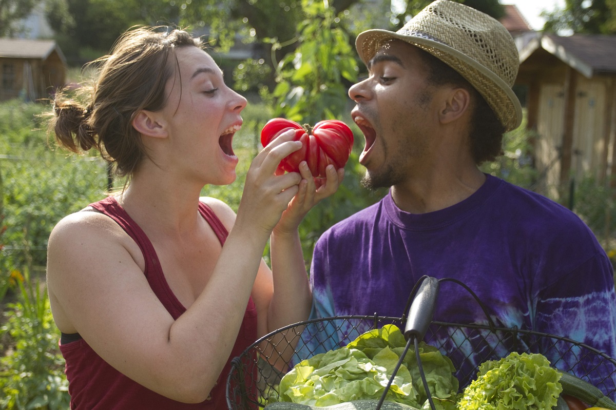 Deux jeunes adultes allant croquer dans une tomate